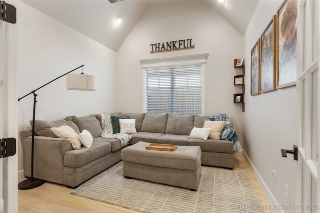 living area featuring light wood-type flooring, high vaulted ceiling, and baseboards