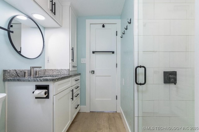 bathroom featuring wood finished floors, a shower stall, vanity, and baseboards