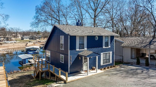 view of front of house featuring a water view, a chimney, a boat dock, and roof with shingles