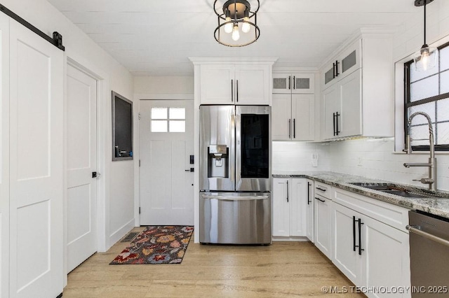 kitchen with light wood-style flooring, stainless steel appliances, a sink, white cabinetry, and light stone countertops