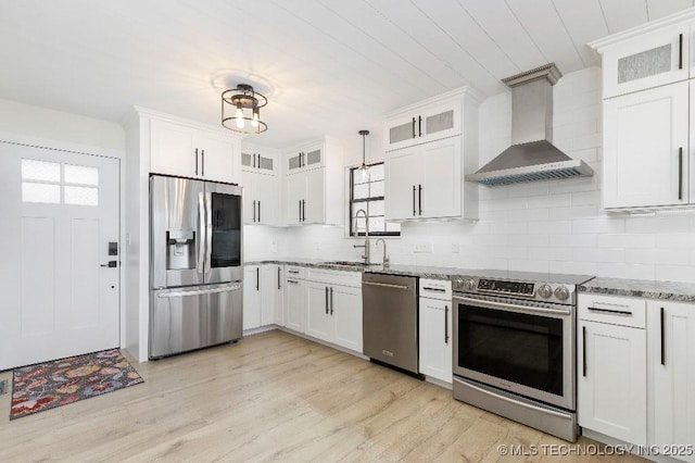 kitchen featuring stainless steel appliances, white cabinetry, light stone countertops, light wood-type flooring, and wall chimney exhaust hood