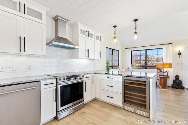 kitchen with white cabinets, wine cooler, appliances with stainless steel finishes, a peninsula, and wall chimney range hood