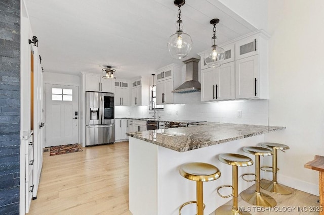 kitchen featuring light wood finished floors, stainless steel fridge, tasteful backsplash, a peninsula, and wall chimney range hood