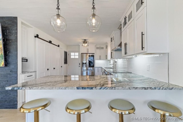 kitchen with a barn door, stainless steel fridge with ice dispenser, wall chimney exhaust hood, glass insert cabinets, and a peninsula