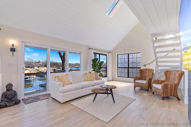 living area featuring high vaulted ceiling, a skylight, and light wood-style flooring