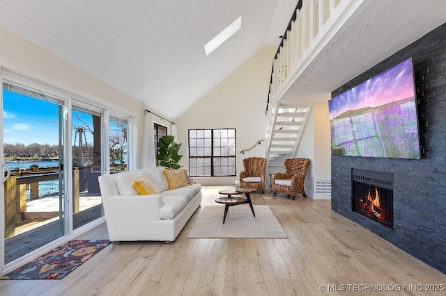 living area featuring a skylight, a water view, a large fireplace, high vaulted ceiling, and light wood-type flooring