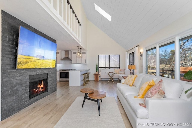 living area with light wood-style floors, a skylight, a warm lit fireplace, and high vaulted ceiling