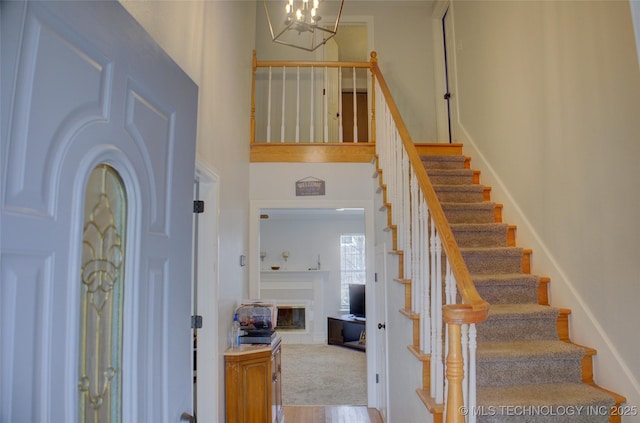 foyer entrance with a towering ceiling, stairway, a chandelier, and a glass covered fireplace