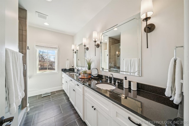 bathroom featuring double vanity, a stall shower, a sink, and visible vents