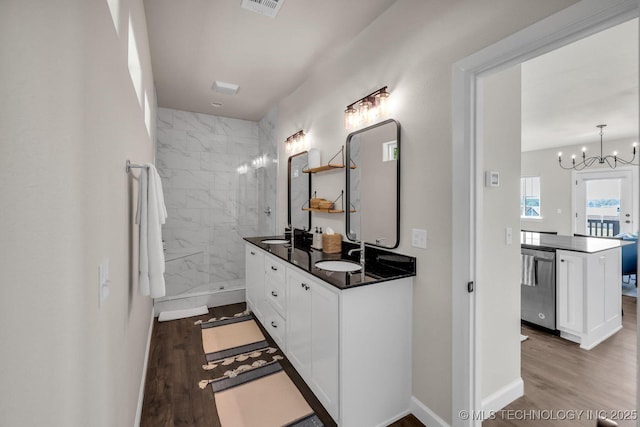 bathroom featuring double vanity, tiled shower, wood finished floors, an inviting chandelier, and a sink