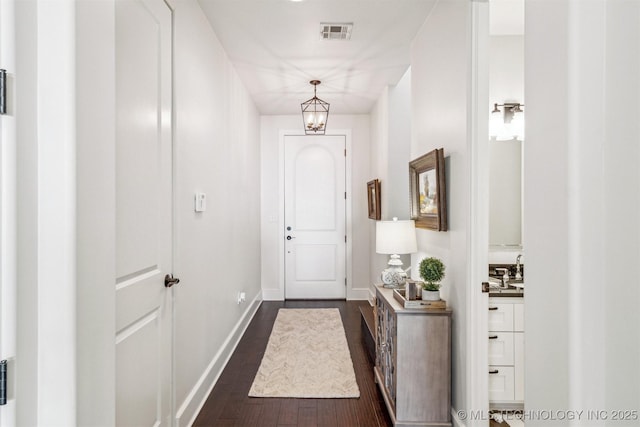 doorway with dark wood-style floors, baseboards, visible vents, and a notable chandelier