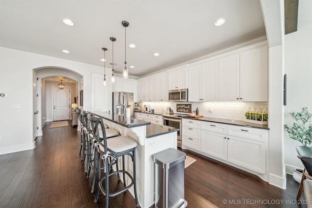 kitchen with arched walkways, stainless steel appliances, a breakfast bar, decorative backsplash, and dark countertops