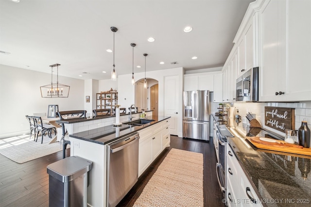 kitchen with arched walkways, stainless steel appliances, dark wood-type flooring, a sink, and decorative backsplash