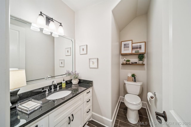 half bath with baseboards, vaulted ceiling, vanity, and toilet