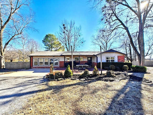 ranch-style house featuring concrete driveway, brick siding, fence, and a patio