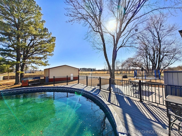 view of swimming pool featuring a trampoline, fence, and an outbuilding