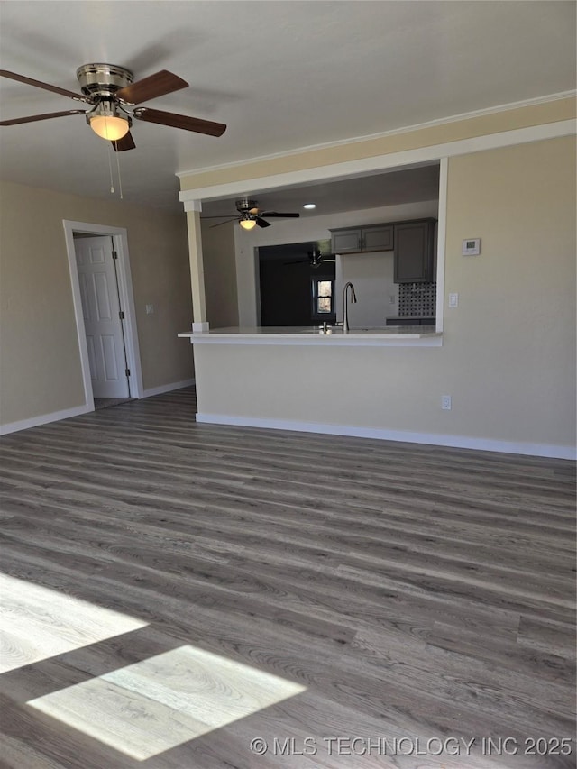 unfurnished living room featuring dark wood-type flooring, a sink, and baseboards