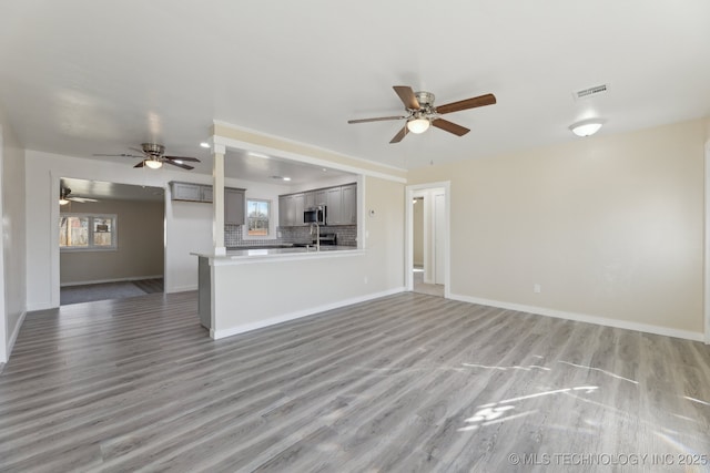 unfurnished living room featuring light wood finished floors, a ceiling fan, visible vents, and baseboards