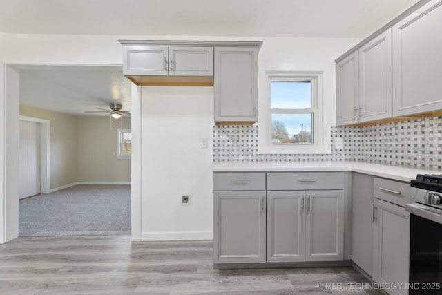 kitchen with tasteful backsplash, baseboards, light countertops, gray cabinetry, and stainless steel range with gas cooktop