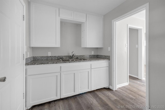 kitchen with stone countertops, white cabinetry, a sink, and wood finished floors