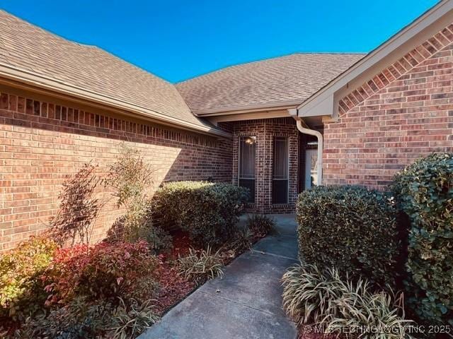 entrance to property featuring a shingled roof and brick siding