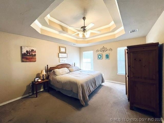 carpeted bedroom with ornamental molding, a tray ceiling, visible vents, and baseboards