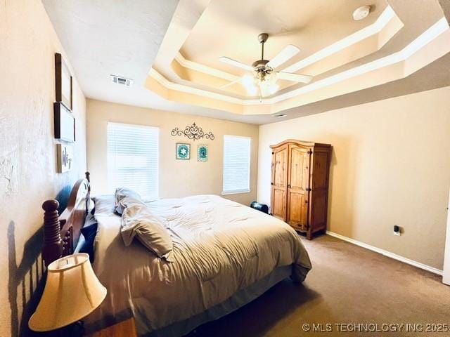 carpeted bedroom featuring a tray ceiling, crown molding, visible vents, ceiling fan, and baseboards