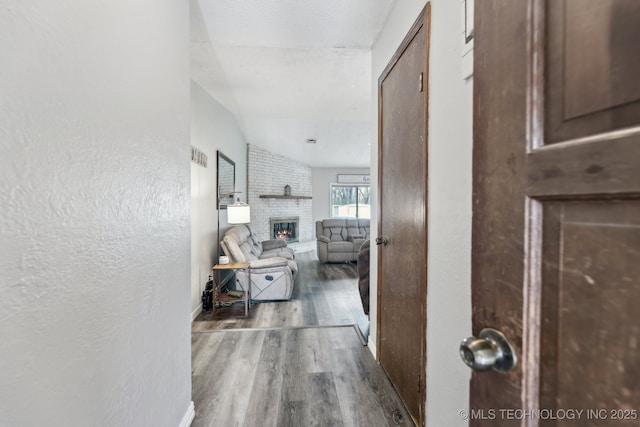 corridor featuring a textured ceiling, a textured wall, wood finished floors, baseboards, and vaulted ceiling