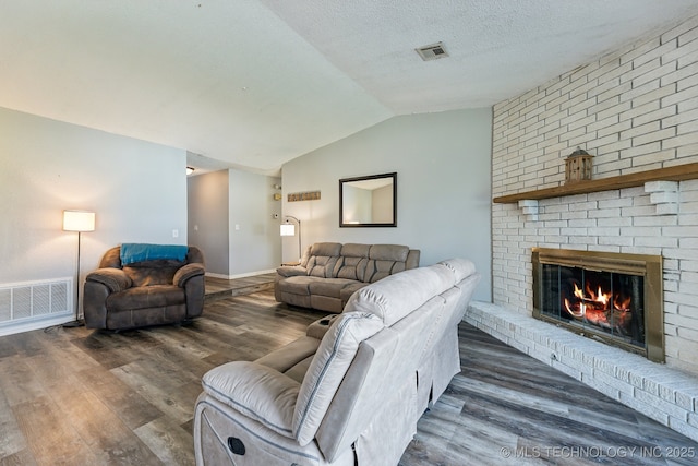 living room featuring lofted ceiling, a fireplace, visible vents, and wood finished floors