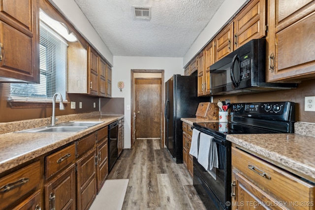 kitchen with visible vents, wood finished floors, a textured ceiling, black appliances, and a sink