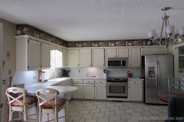 kitchen featuring appliances with stainless steel finishes, light countertops, a sink, and a peninsula