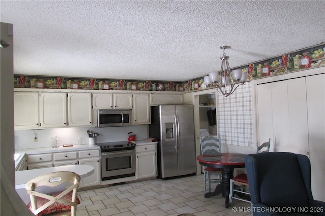 kitchen with appliances with stainless steel finishes, hanging light fixtures, light countertops, a textured ceiling, and a notable chandelier