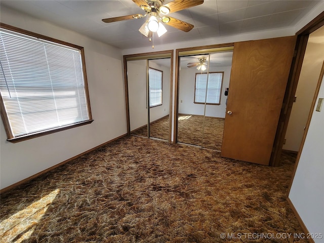 unfurnished bedroom featuring baseboards, multiple windows, a ceiling fan, and multiple closets