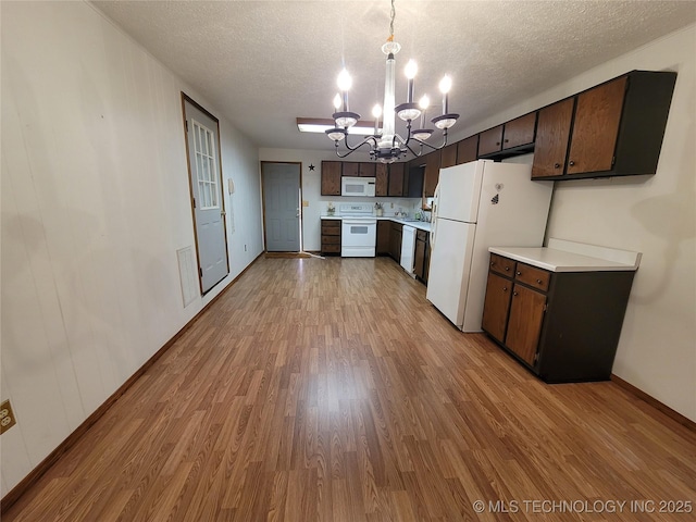 kitchen with a textured ceiling, a notable chandelier, white appliances, wood finished floors, and light countertops