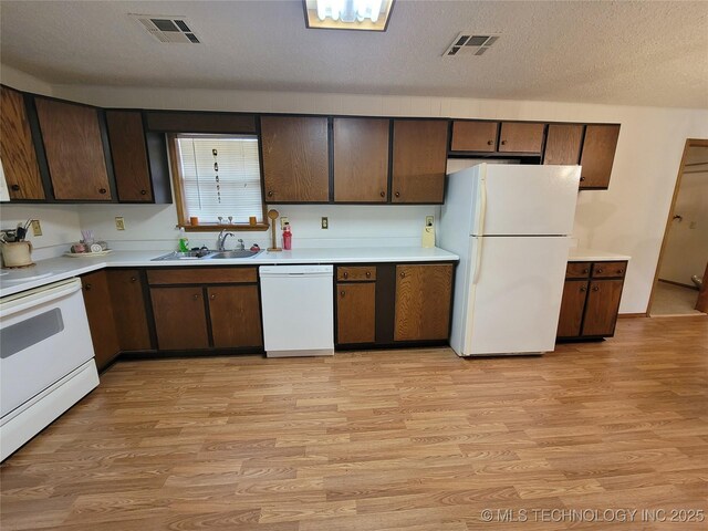 kitchen with light wood finished floors, light countertops, visible vents, a sink, and white appliances
