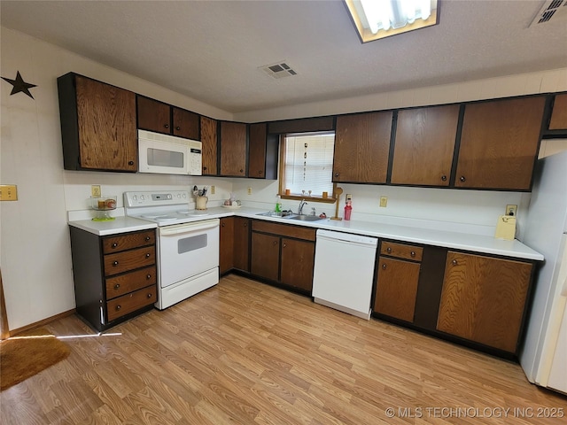 kitchen with white appliances, visible vents, light wood-style floors, and a sink