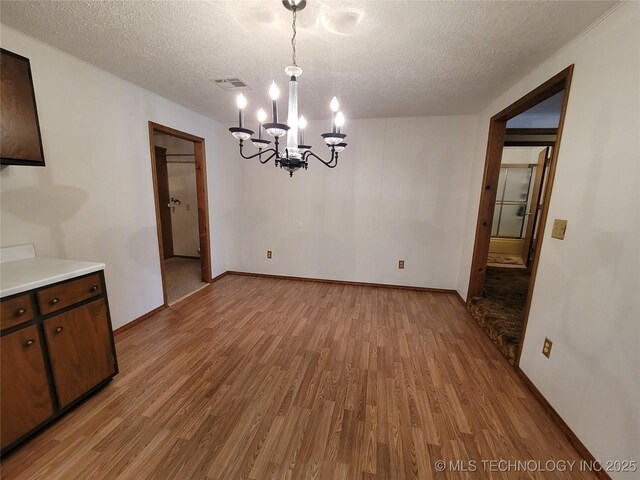 unfurnished dining area with a chandelier, visible vents, a textured ceiling, and light wood finished floors