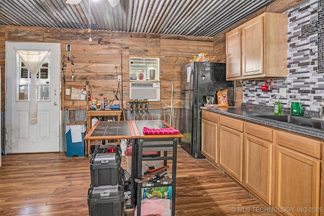 kitchen featuring dark countertops, dark wood-style floors, freestanding refrigerator, wood walls, and a sink