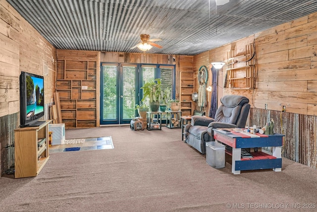 carpeted living area with ceiling fan and wooden walls