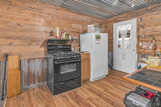 kitchen with wood walls, light wood-type flooring, black gas range, and freestanding refrigerator