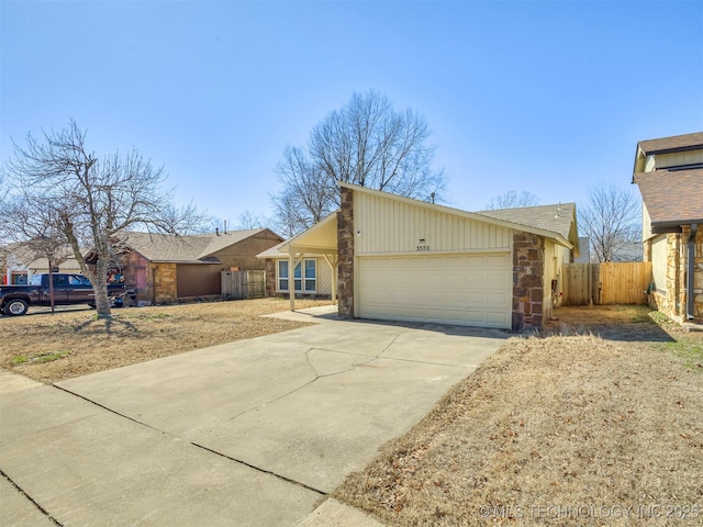 view of front facade with an attached garage, stone siding, fence, and concrete driveway