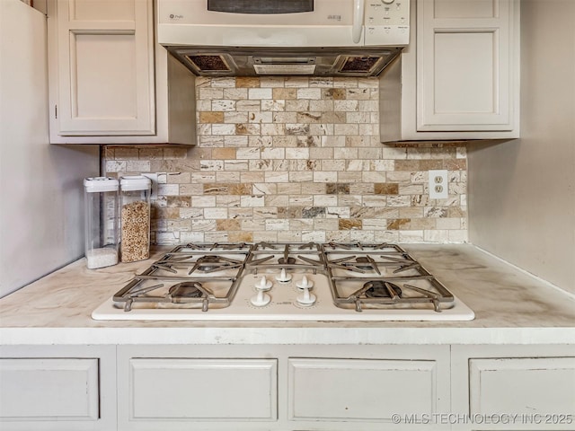 kitchen featuring white appliances, under cabinet range hood, light countertops, and decorative backsplash