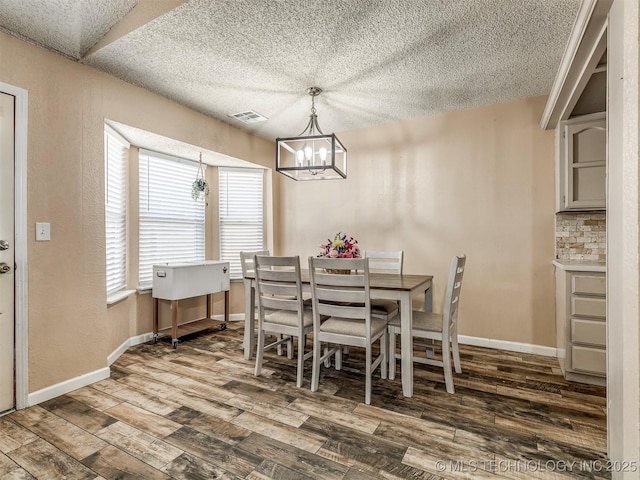 dining area with a textured ceiling, wood finished floors, visible vents, and baseboards