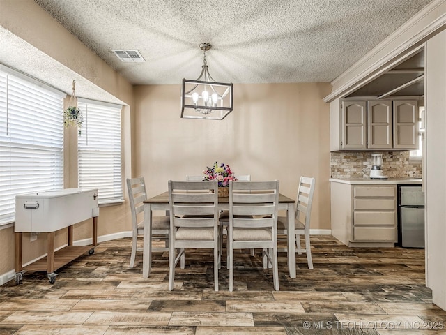 dining room with a textured ceiling, wood finished floors, visible vents, and a notable chandelier