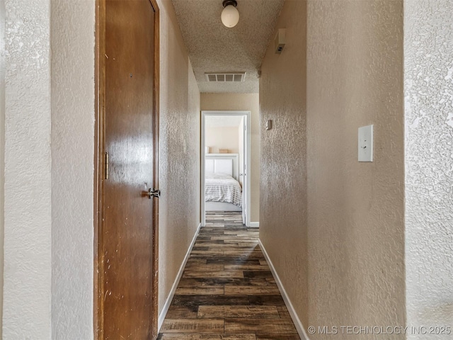 corridor featuring a textured ceiling, a textured wall, dark wood finished floors, and visible vents