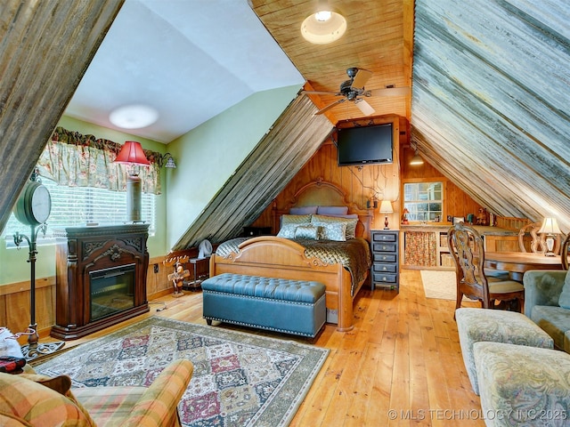 bedroom featuring lofted ceiling, wood-type flooring, a glass covered fireplace, and wooden walls