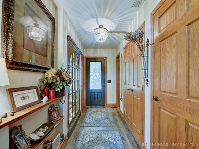 foyer with light wood-style floors, visible vents, baseboards, and an inviting chandelier