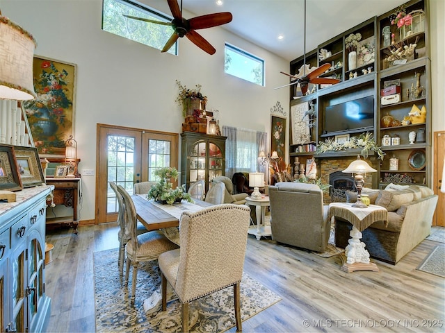 dining area featuring a stone fireplace, light wood finished floors, a towering ceiling, and a healthy amount of sunlight