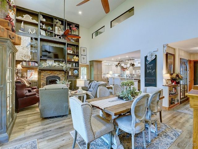 dining area with light wood finished floors, a fireplace, a high ceiling, and a ceiling fan