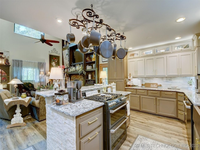 kitchen featuring ceiling fan, stainless steel appliances, open floor plan, light stone countertops, and light wood finished floors